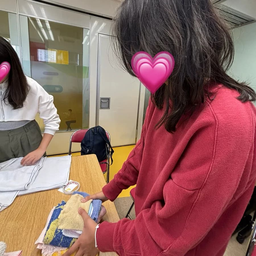 A volunteer in a red jumper sorting through card materials at a work table. Faces are covered with heart stickers.