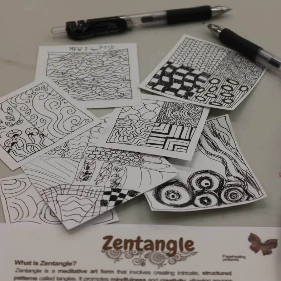 A Zentangle worksheet on a desk, covered in intricate black and white pattern drawings, with two pens beside it.